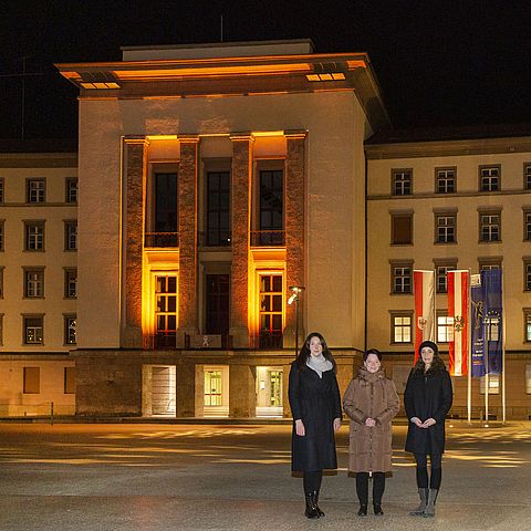 LTPin Sonja Ledl-Rossmann (Mitte), VPin Sophia Kircher und LRin Eva Pawlata vor dem orange beleuchteten Landhaus 1
