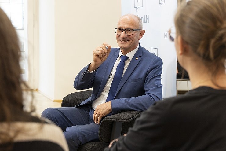 Ein Mann in blauem Anzug gestikuliert mit der rechten Hand.