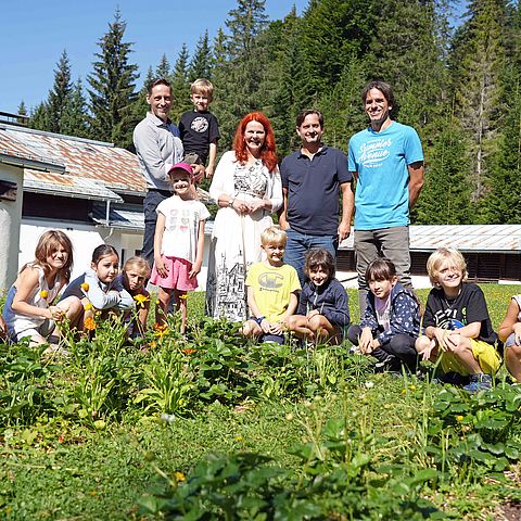 Clemens Mair, LRin Cornelia Hagele, Michael Steinlechner und Christian Biendl zusammen mit einer Gruppe Kindern auf einer Wiese.