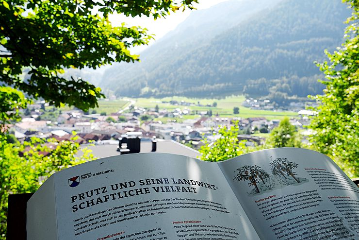 Aufgeschlagenes Buch zur landwirtschaftlichen Vielfalt in Prutz vor Blick über Gemeinde