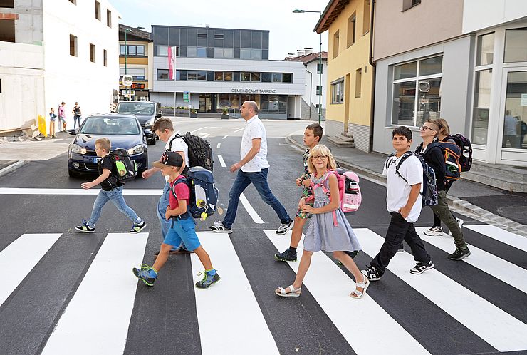 Mann und Kinder mit Schultaschen gehen über Zebrastreifen