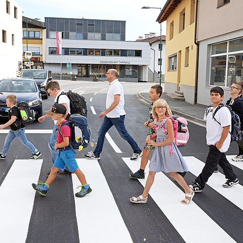 Mann und Kinder mit Schultaschen gehen über Zebrastreifen