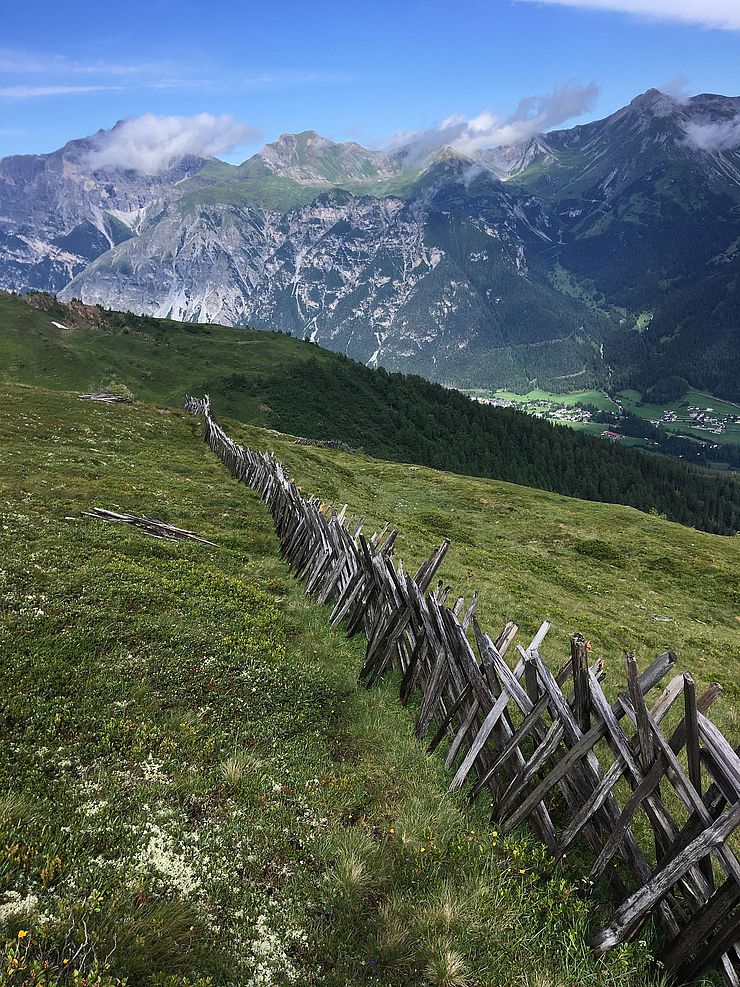 Eine Wiese mit einem Holzzaun und einer traumhaften Bergkulisse im Hintergrund.