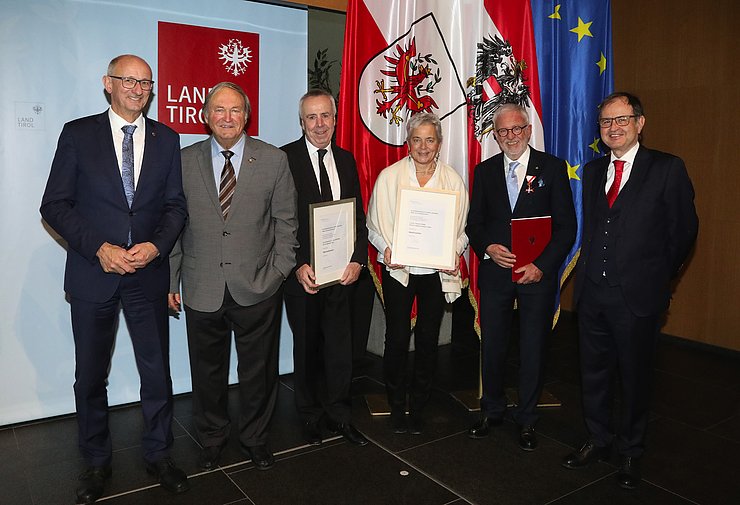 Sechs Personen stehen auf einer Bühne vor einer Fahne.