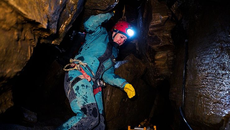 LRin Mair in Höhle mit Schutzanzug, Helm und Stirnlampe kletternd