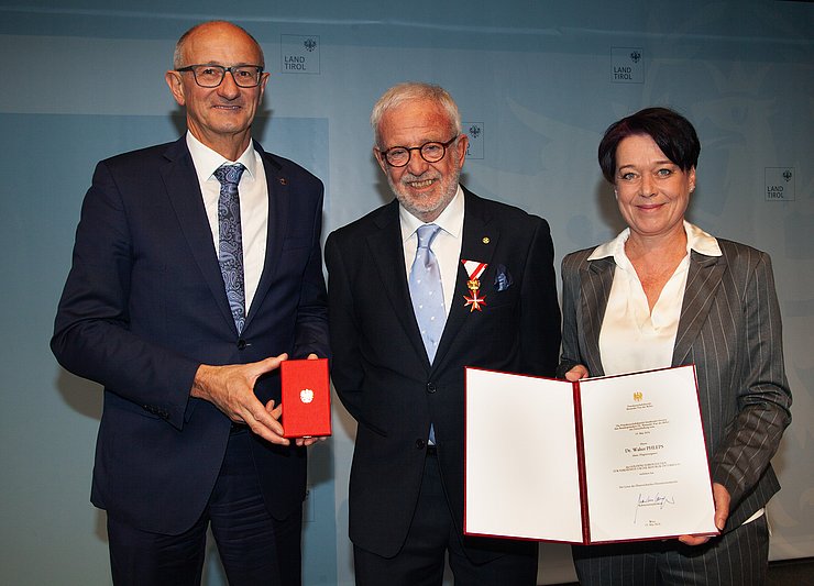 Landeshauptmann Mattle und Landtagspräsidentin Ledl-Rossmann übergeben eine Urkunde an einen Mann.