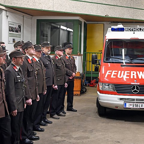 Gruppe Feuerwehrleute in Formation stehend; daneben Feuerwehrauto