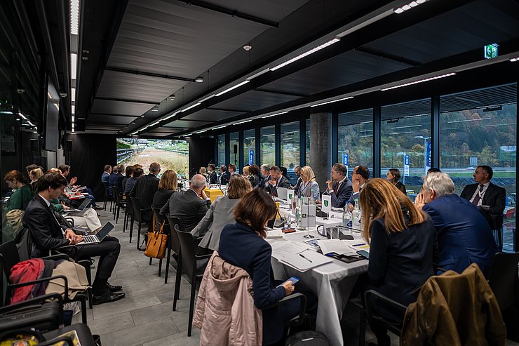 Saal mit Personen, die an Besprechungstisch sitzen