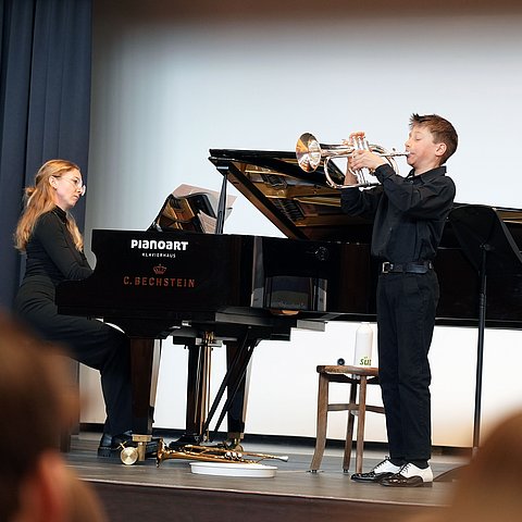 Ein junger Bub spielt Flügelhorn, neben ihm sitzt eine Frau am Klavier.