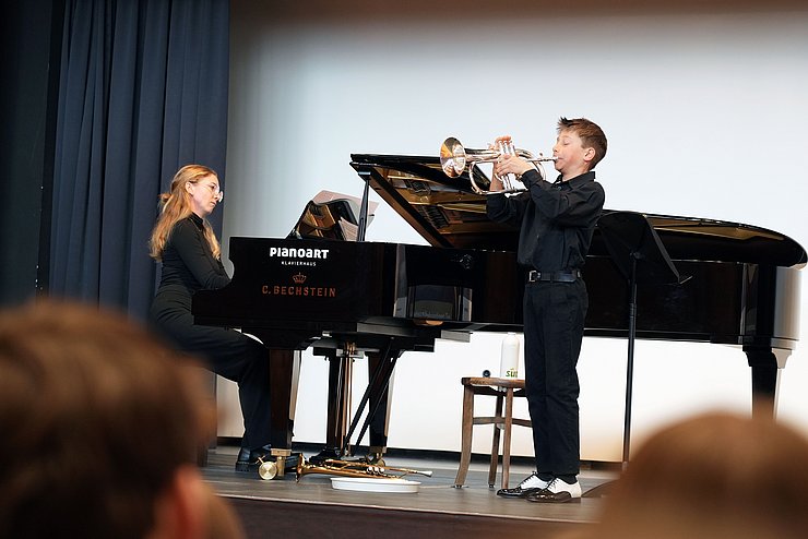 Ein junger Bub spielt Flügelhorn, neben ihm sitzt eine Frau am Klavier.