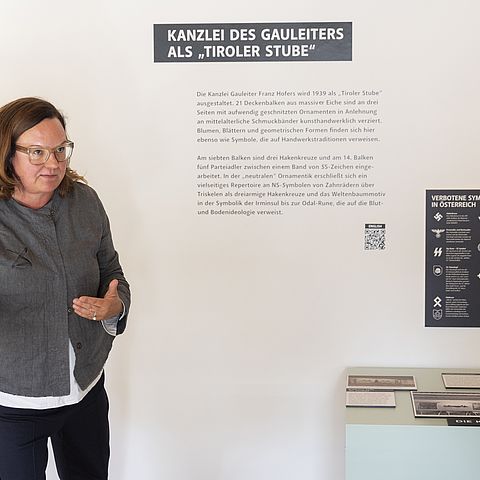 Eine Frau vor einer Wand im Ausstellungsraum, die beschriftet ist.