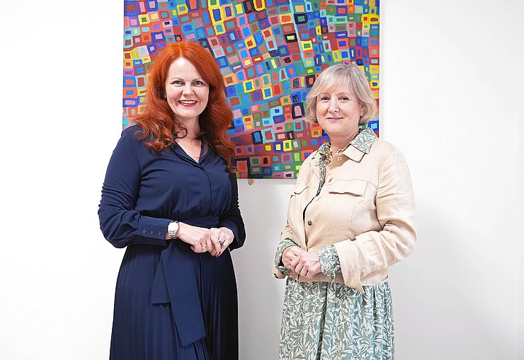 © Land Tirol/Hörmann LRin Cornelia Hagele zusammen mit der ausgezeichneten Gabriele Lehner vor einem Gemälde mit bunten Vierecken.