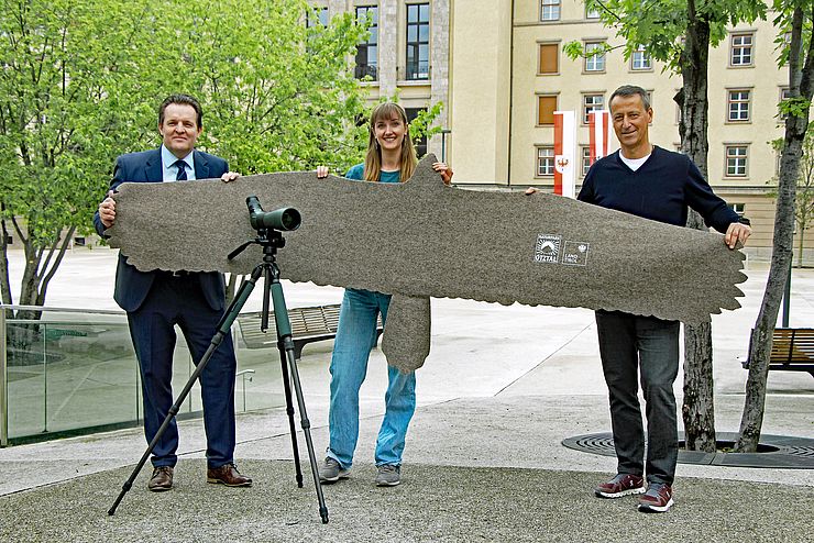 Drei Personen halten große Filzabbildung in der Hand 