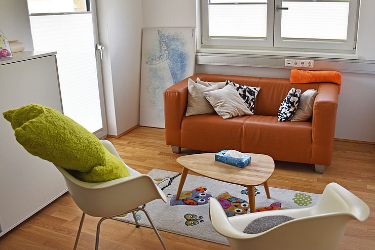Beratungsraum mit oranger Couch, zwei Stühlen und Polstern