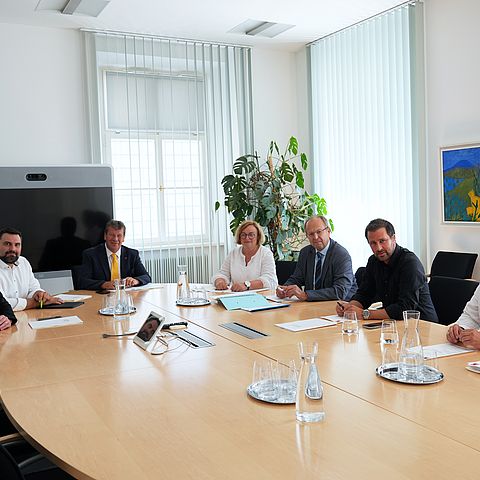 Die Mitglieder des Wohnbauförderungskuratoriums sitzen bei ihrer jüngsten Sitzung im Landhaus in Innsbruck um einen ovalen Tisch schauen für das Gruppenfoto in die Kamera