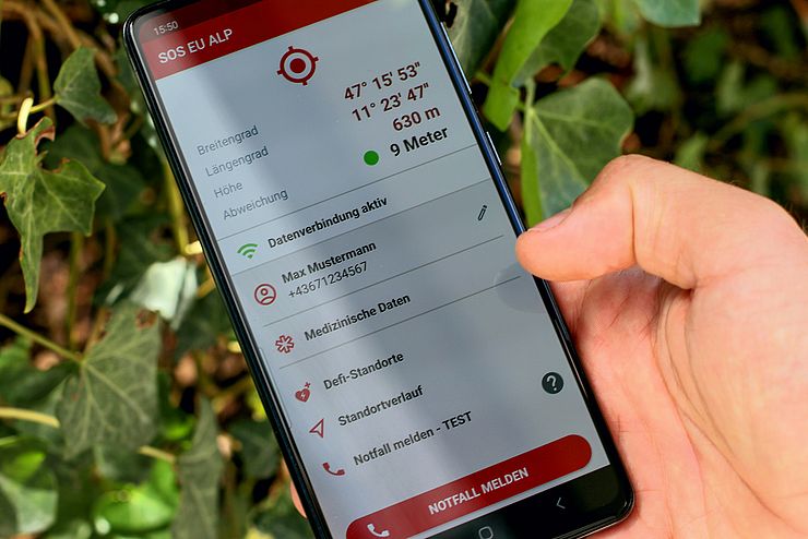 Eine Hand hält ein Smartphone, auf dem die SOS-EU-ALP App geöffnet ist.