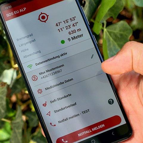 Eine Hand hält ein Smartphone, auf dem die SOS-EU-ALP App geöffnet ist.