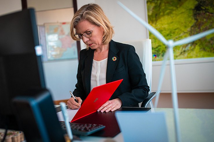 Eine Frau sitzt an einem Schreibtisch und unterzeichnet ein Dokument. 