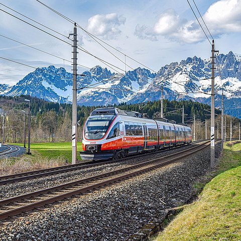 Eine ÖBB-Zuggarnitur fährt auf Gleisen, im Hintergrund sieht man Berge.