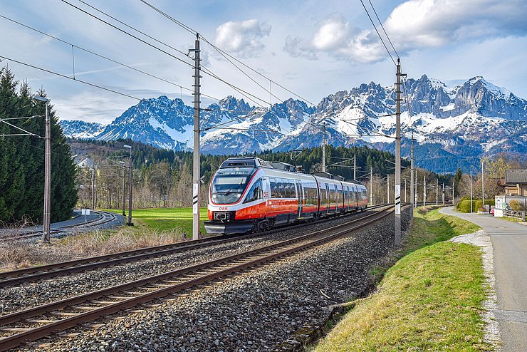 Eine ÖBB-Zuggarnitur fährt auf Gleisen, im Hintergrund sieht man Berge.