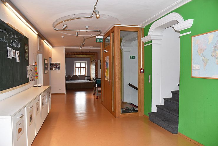 Bereich hinter dem Eingang/Flur - an der grünen Wand hängt eine Weltkarte, gegenüber befindet sich eine Kommode und eine Tafel, Treppe führt nach oben