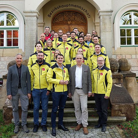 Gruppenfoto vor der BH; fast alle tragen gelbe Einsatzjacken