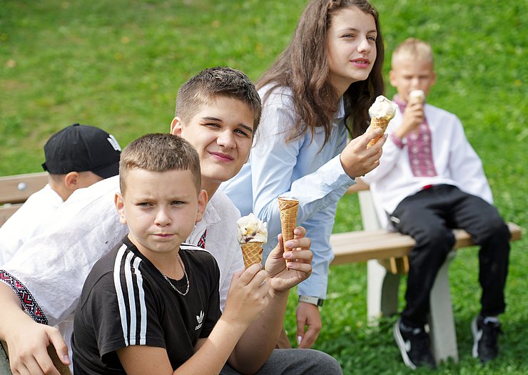 Mehrere Kinder sitzen mit Eistüten auf einer Bank.