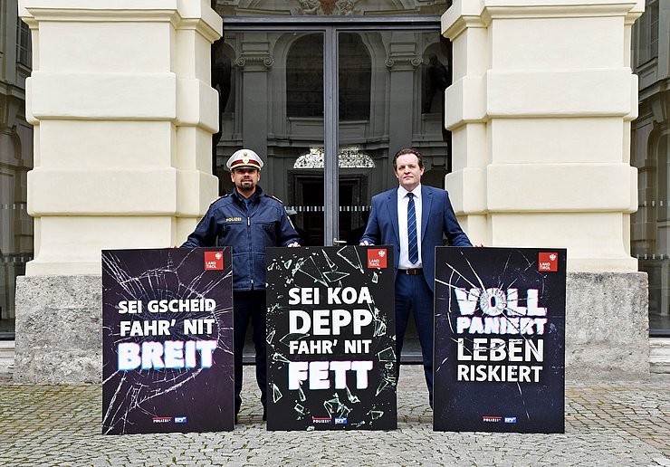 © Land Tirol/Neuner Ein Polizist und ein Mann im Anzug mit drei Plakaten