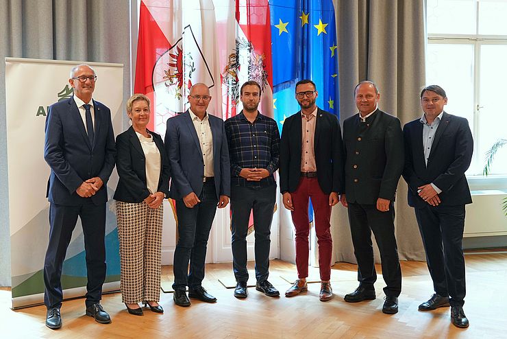 Personen stehen nebeneinander, dahinter Fahnen und ARGE-ALP-Rollup