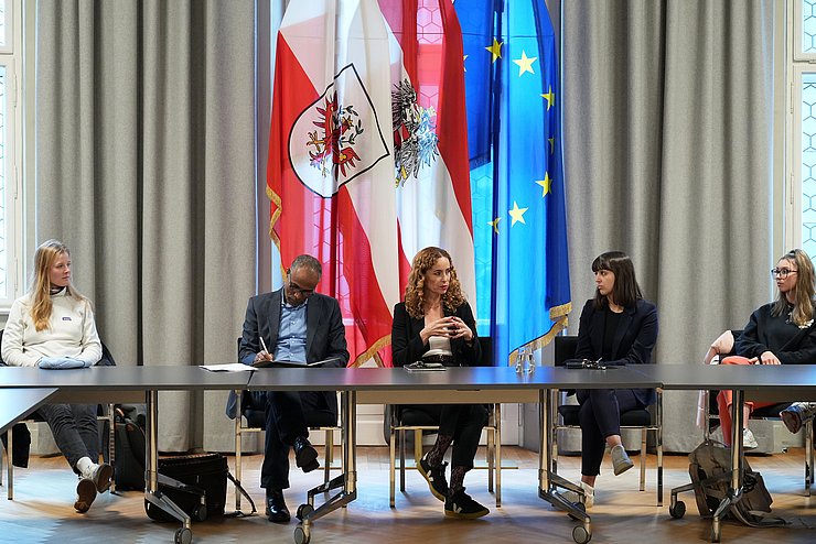 Personen sitzen an Tisch - Landesrätin beim Sprechen