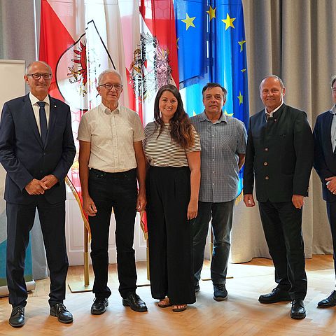 Personen stehen nebeneinander, vor Fahnen und ARGE-ALP-Rollup