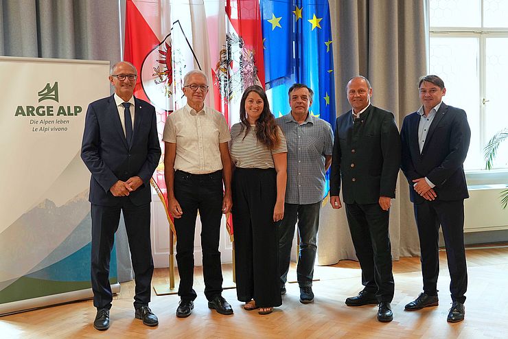 Personen stehen nebeneinander, vor Fahnen und ARGE-ALP-Rollup