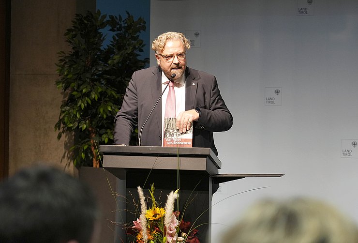 Ein Mann mit Locken und einem Bart steht an einem Rednerpult.