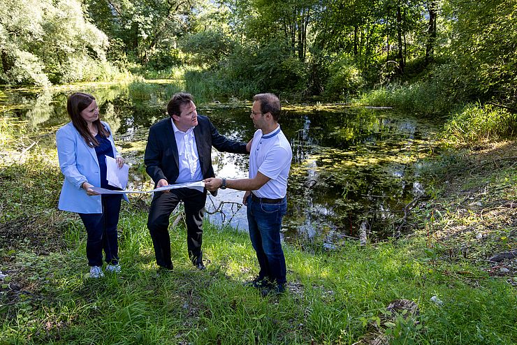 Holzer, Zumtobel und Guggenberger schauen sich das Projekt auf einer Karte an. Im Hintergrund ist der Teich zu sehen.