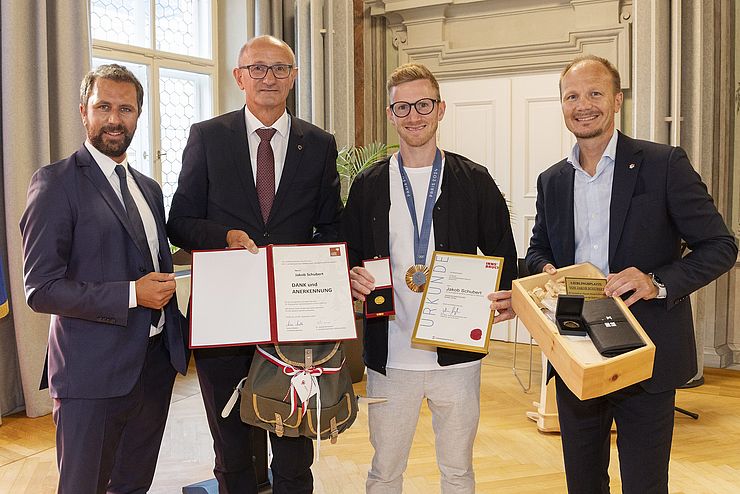 Vier Männer haben sich nebeneinander aufgestellt und halten die Urkunden und Geschenke vor die Kamera. 