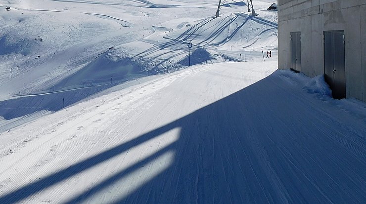 Schnee, Schispuren, Schatten einer Seilbahnstütze, im Vordergrund Seilbahnstation