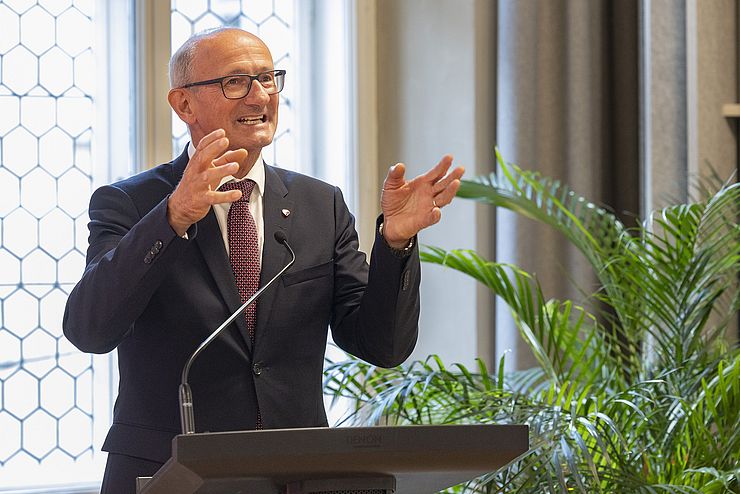 Ein weiterer Mann hinter dem Rednerpult gestikuliert, diesmal mit beiden Händen.