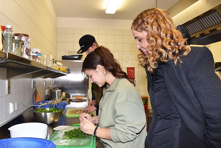 LRin schaut Mädchen beim Gemüseschneiden in der Küche über die Schulter