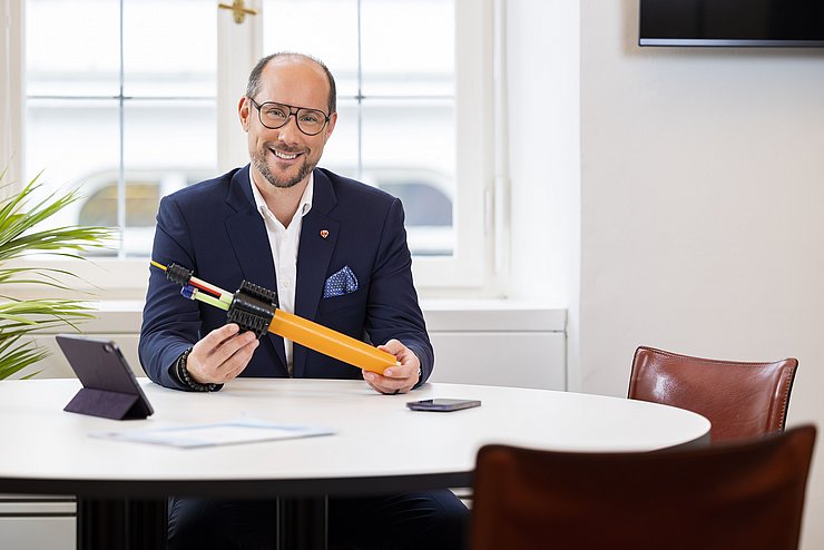 Mann sitzt am Tisch und hält Breitbandkabel in der Hand