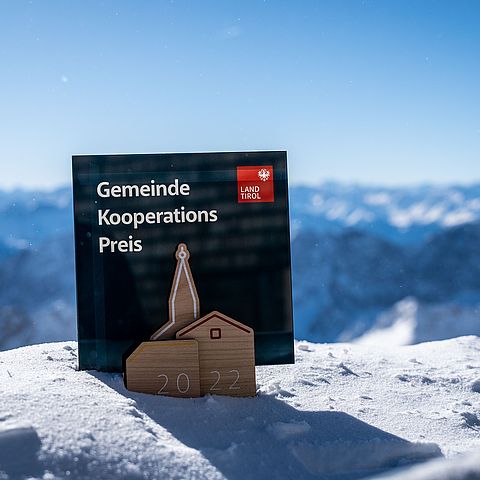 Pokal des GEKO auf Schnee stehend mit Bergen im Hintergrund