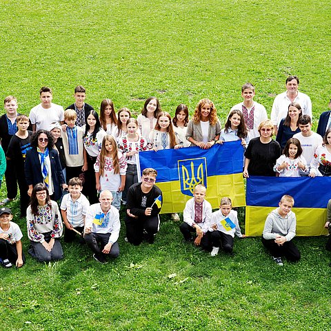 Gruppenaufnahme von Kindern und einigen Erwachsenen, zu sehen sind auch ukrainische Flaggen.