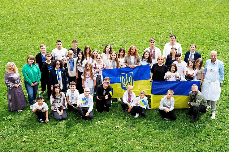 Gruppenaufnahme von Kindern und einigen Erwachsenen, zu sehen sind auch ukrainische Flaggen.