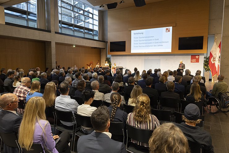 Ein großer Saal gefüllt mit vielen Gästen vor einer Bühne.