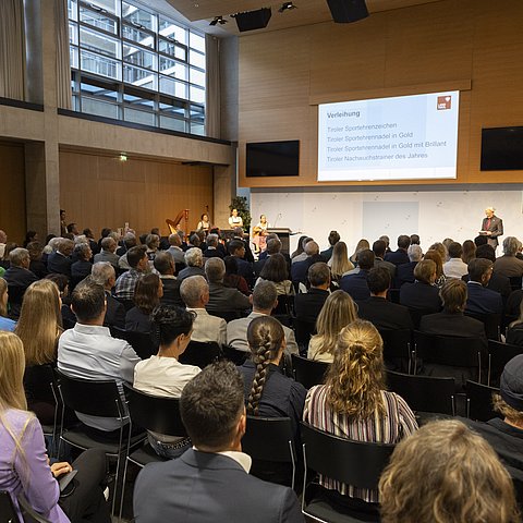 Ein großer Saal gefüllt mit vielen Gästen vor einer Bühne.