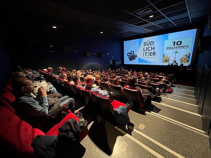 Voll besetzter Kinosaal, vorne auf der Leinwand: Titelbild des Films "10 Milliarden"