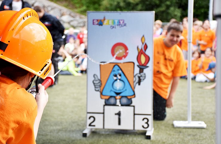 © Land Tirol/Neuner Ein Bub zielt mit dem Schlauch auf die Zieltafel, dahinter schaut ein anderer Schüler hervor.