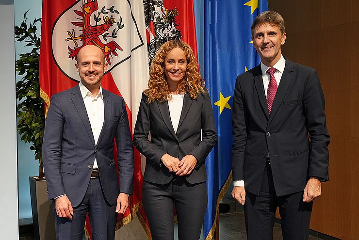 Personen stehen nebeneinander, vor Fahnen