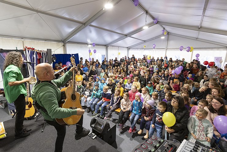 Bühne mit Sänger, der Gitarre spielt. Im Hintergrund Publikum